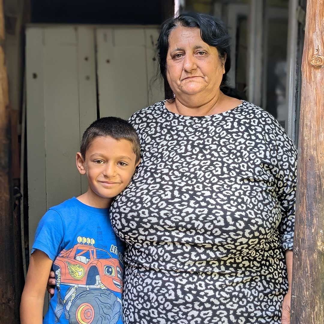 A woman and child stand outside their house.