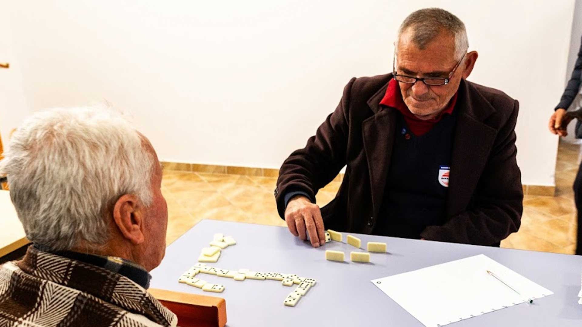 Misir, an elderly man, smiles as he plays dominoes with a church friend.
