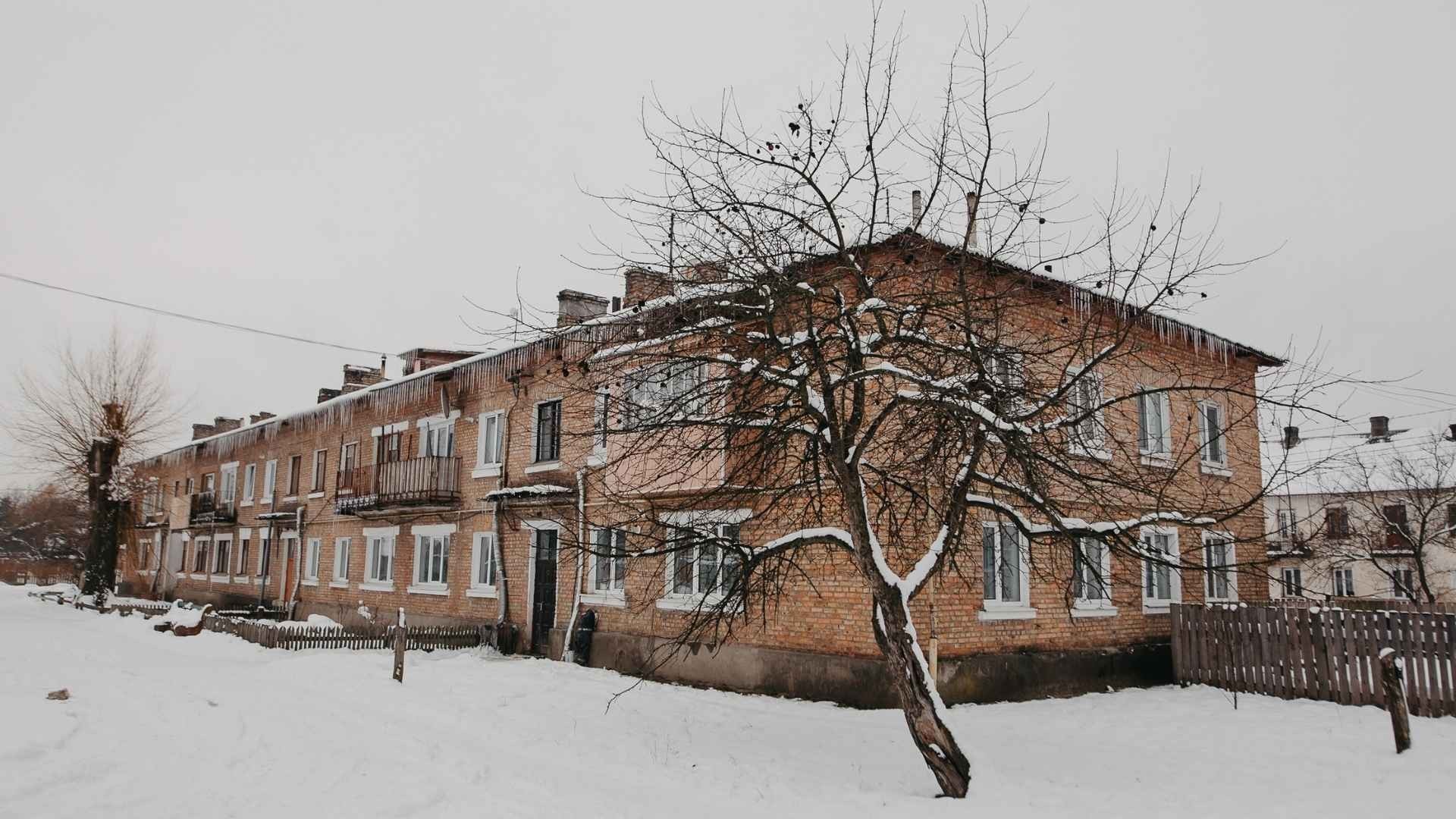 Snow-covered apartment block stands in deep winter, under a cold grey sky