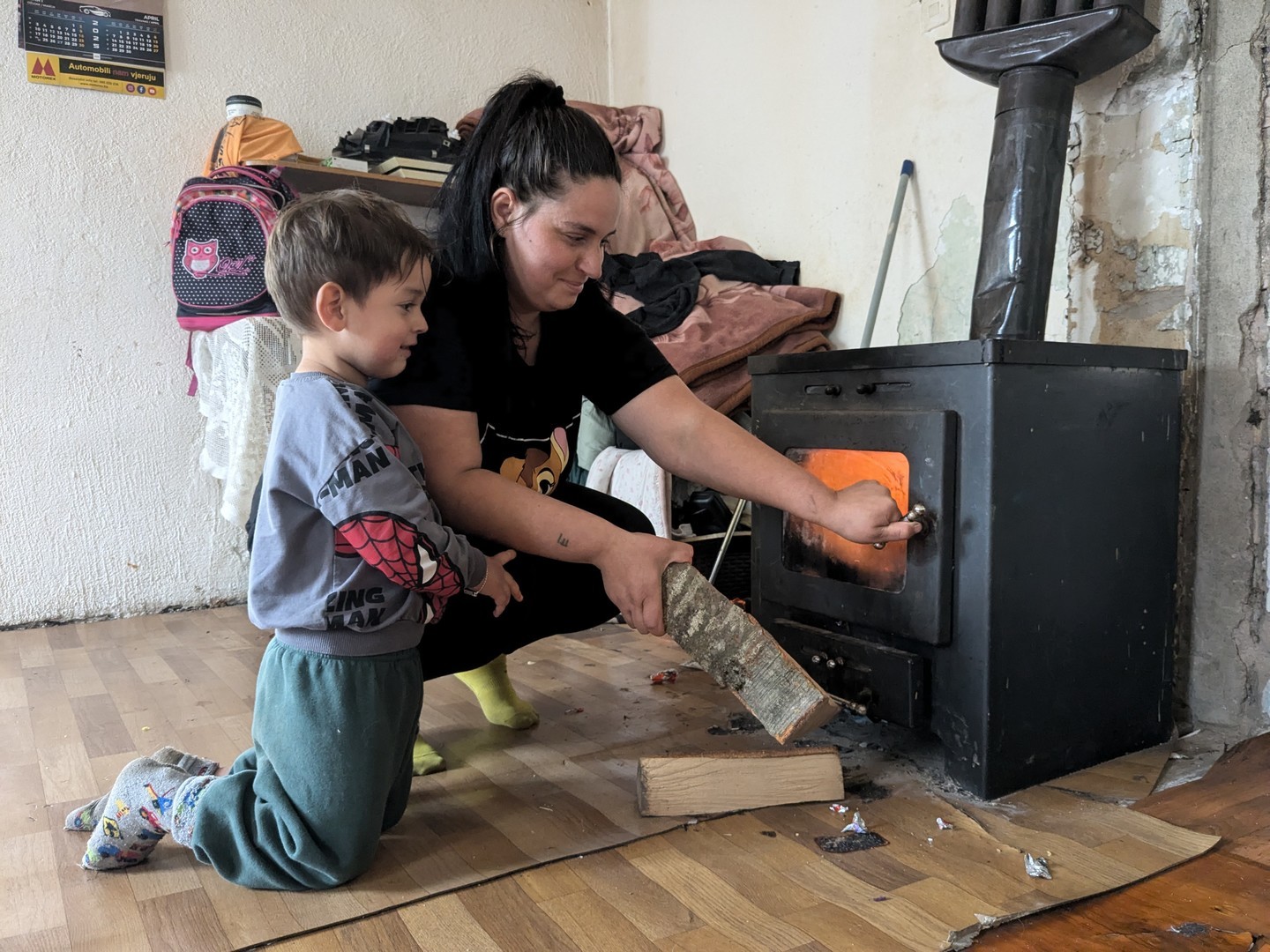 Mom and Adil load the stove with wood to heat the house.